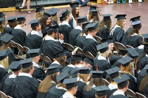 students sitting at high school graduation in graduation gowns