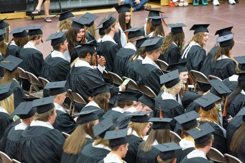 high school graduation students sitting at high school graduation in graduation gowns