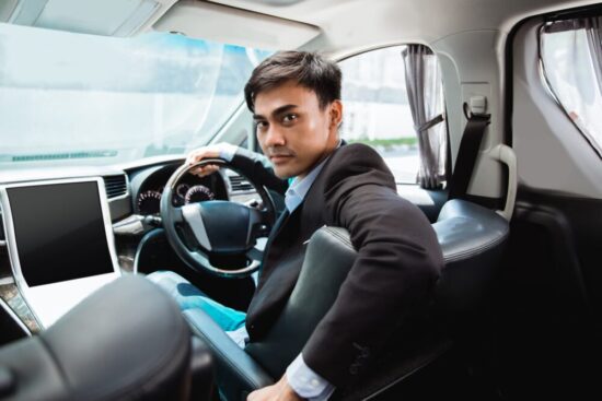 Man in the driver's seat wearing a suit, looking back at the passenger.