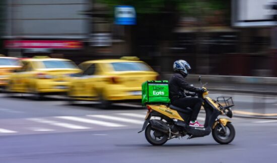 Person on a scooter with an Uber Eats green box on his back as he drives through the city.