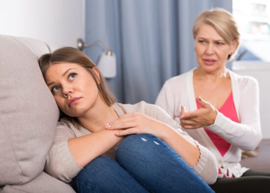 Young woman is leaning her head against the couch with her back to her elderly mother who is having a serious discussion with her.