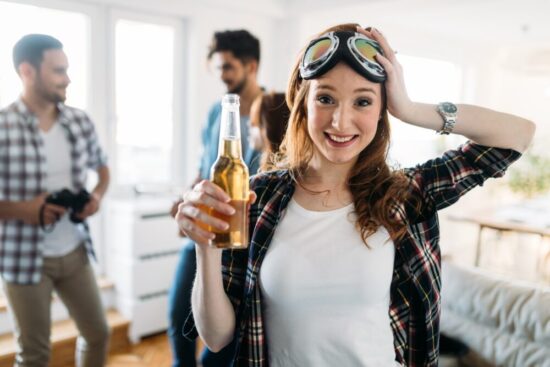 Young woman holding a beer at a get together while two young men behind her talk