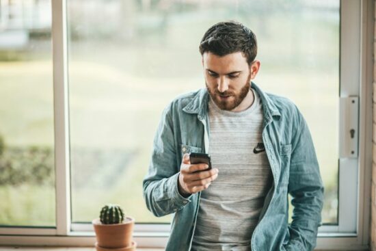 Man using his cell phone. He is sitting on a window sill.