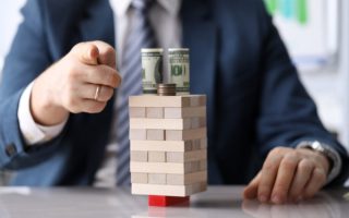 do debt consolidation programs work - man pointing at the camera over Jenga puzzle with money balanced on top